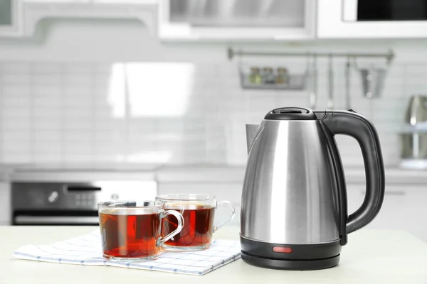 Hervidor eléctrico moderno y tazas de té en la mesa de madera blanca en la cocina. Espacio para texto —  Fotos de Stock