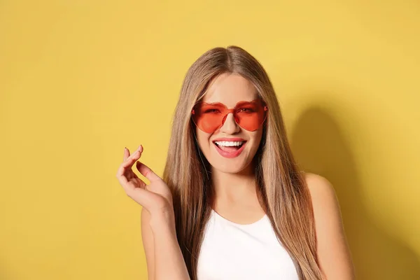 Mujer joven con elegantes gafas de sol en forma de corazón sobre fondo amarillo —  Fotos de Stock