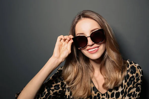 Jeune femme portant des lunettes de soleil élégantes sur fond gris foncé — Photo