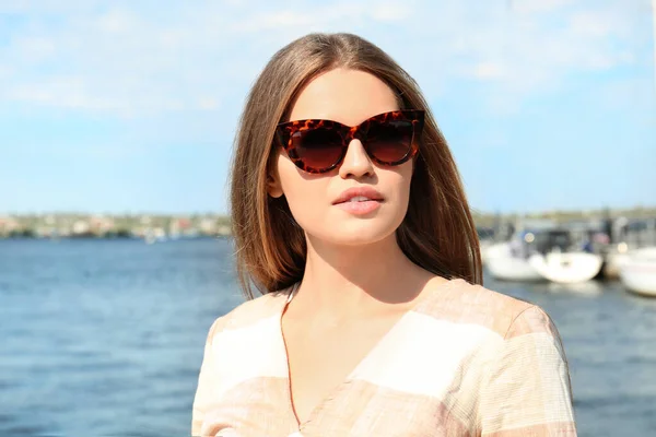 Jeune femme portant des lunettes de soleil élégantes près de la rivière — Photo