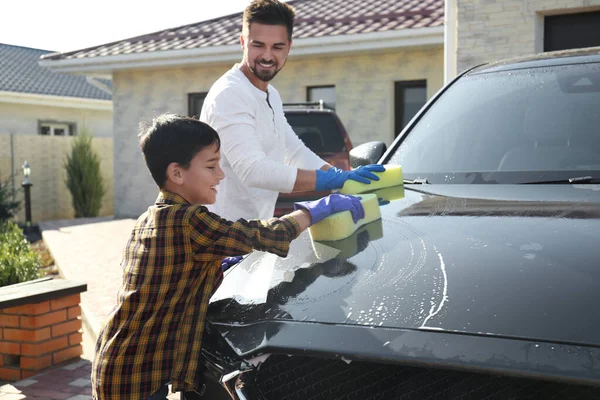 Dad and son washing car at backyard on sunny day