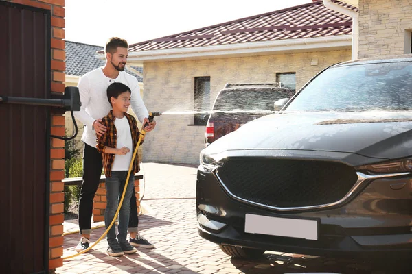 Dad and son washing car at backyard on sunny day