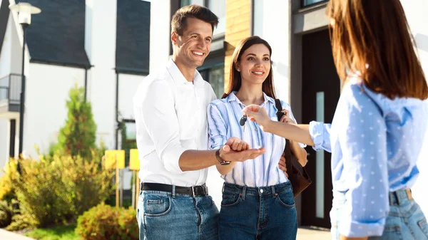 Immobilienmakler übergibt Hausschlüssel an junges Paar — Stockfoto