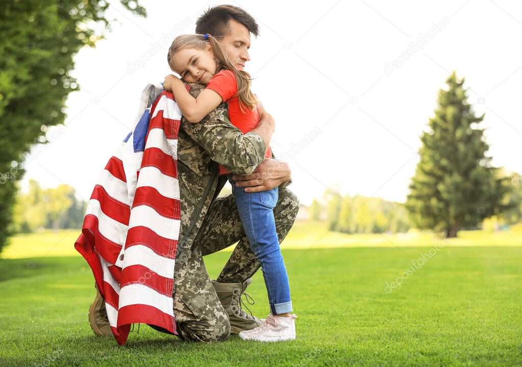 Father in military uniform with American flag hugging his daughter at sunny park