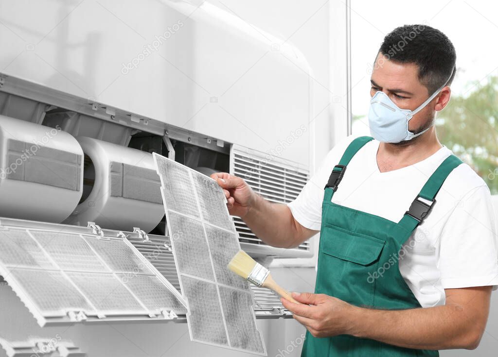 Professional male technician cleaning air conditioner indoors. Repair and maintenance