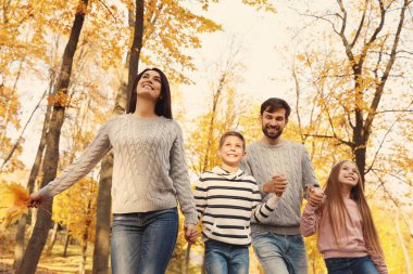 Sonbahar parkında yürüyen çocuklu mutlu bir aile.