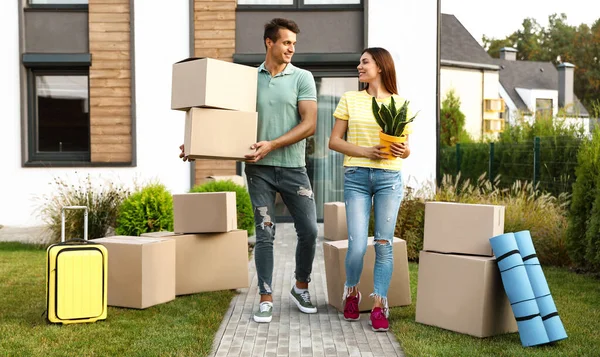 Happy couple with moving boxes and household stuff near their new house on sunny day