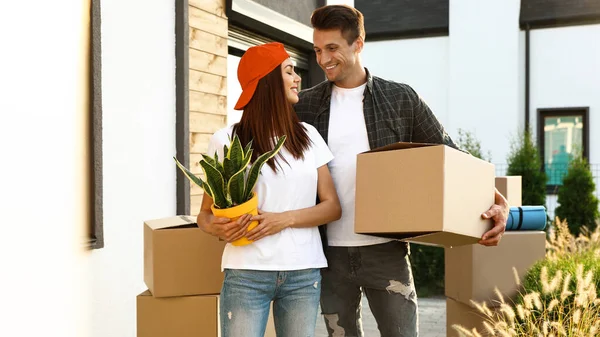 Glückliches Paar mit Umzugskartons und Hausrat in der Nähe seines neuen Hauses am sonnigen Tag — Stockfoto