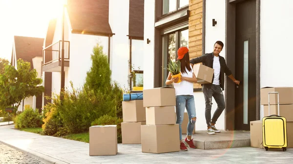 Happy couple with moving boxes and household stuff near their new house on sunny day