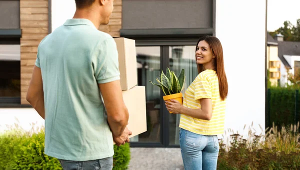 Couple walking to their new house with moving boxes and household stuff