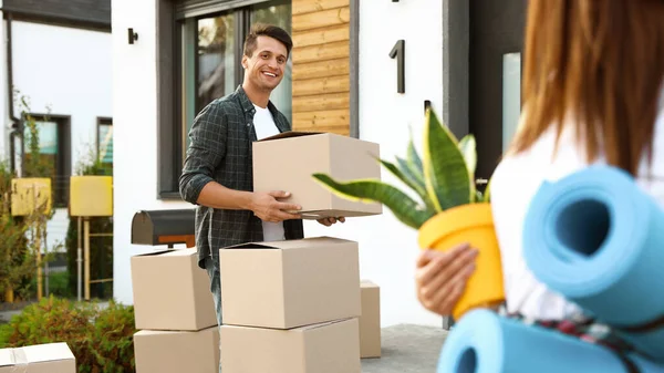 Glückliches Paar mit Umzugskartons und Hausrat in der Nähe seines neuen Hauses am sonnigen Tag — Stockfoto