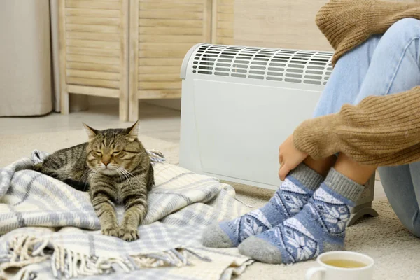 Young woman and cute tabby cat near electric heater at home, closeup — Stock Photo, Image