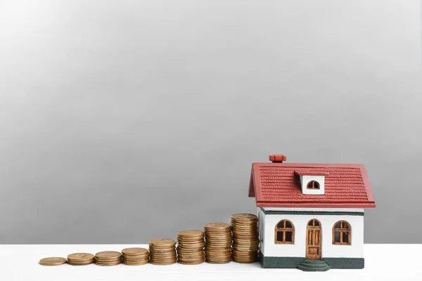 Modelo de casa y monedas sobre mesa de madera blanca sobre fondo gris claro. Ahorro de dinero —  Fotos de Stock