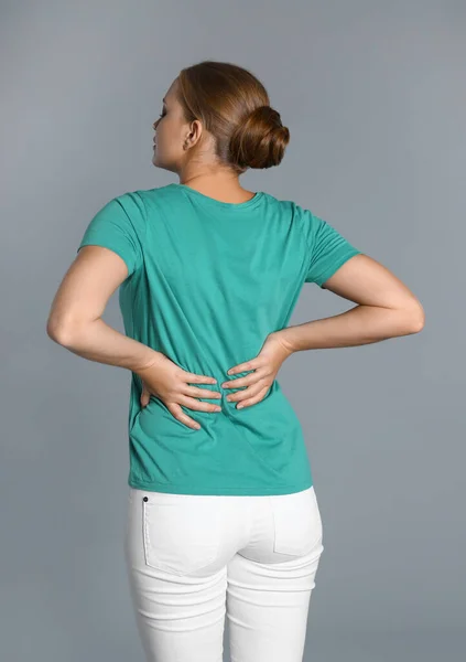 Mujer que sufre de dolor de espalda sobre fondo gris —  Fotos de Stock