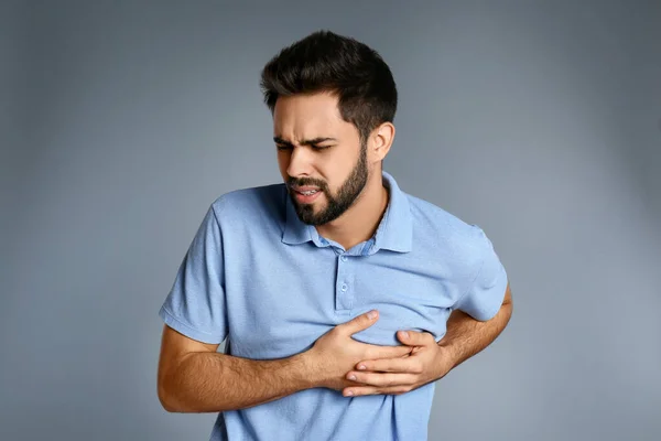 Hombre que sufre de dolor de corazón sobre fondo gris — Foto de Stock