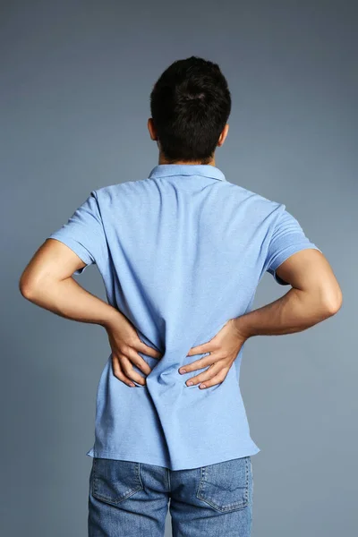 Człowiek cierpi na ból pleców na szarym tle — Zdjęcie stockowe