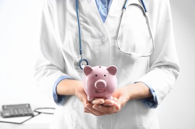 Doctor holding piggybank indoors, closeup. Medical insurance concept