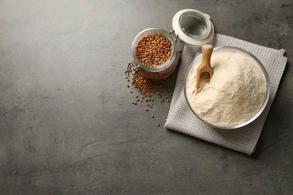 Flat lay composition with bowl of buckwheat flour and grains on grey table, space for text — Stockfoto