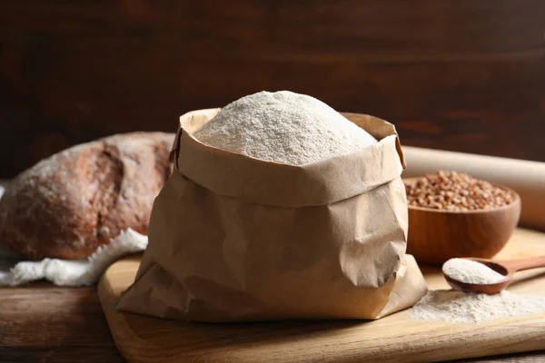Board with paper bag and spoon of buckwheat flour on table — Stock Photo, Image