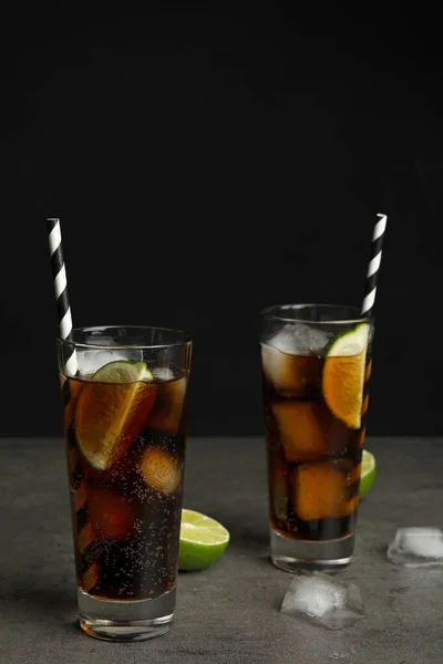 Üdítő szóda italok szalmaszálakkal a szürke asztalon fekete háttér mellett, szöveges hely — Stock Fotó