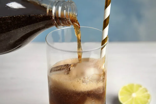 Pouring refreshing soda drink into glass with ice cubes and straw on table, closeup — Stock Fotó