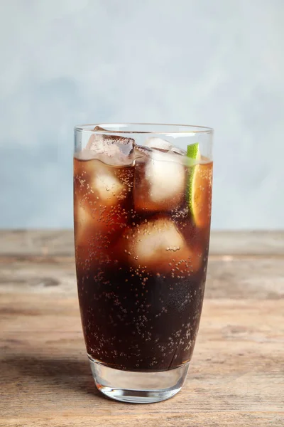 Vaso de refrescante bebida de soda con hielo y lima sobre mesa de madera sobre fondo azul — Foto de Stock