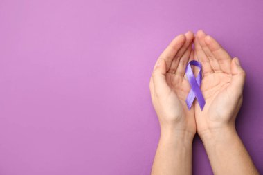 Eflatun arka planda mor kurdele tutan bir kadın. Üstü açık, yazı için yeri olan bir kadın. Aile içi şiddet farkındalığı