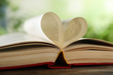 Kalbin ahşap masadaki kitap sayfalarından yapılmış. Arka plan bulanık, yakın plan.