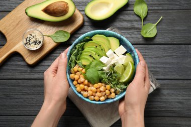 Elinde bir kâse lezzetli avokado salatası ve siyah ahşap masada nohut tutan kadın.