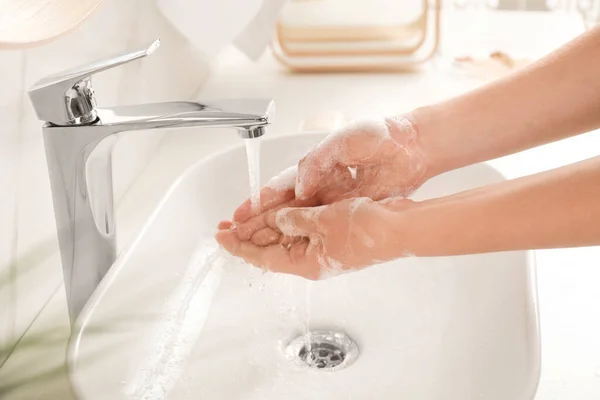 Mujer joven lavándose las manos con jabón sobre el lavabo en el baño, primer plano — Foto de Stock