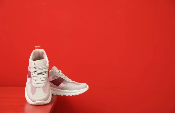 Stylish women's sneakers on wooden table near red wall, space for text — Stock Photo, Image