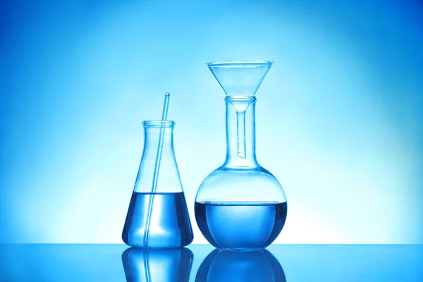 Objectos de vidro de laboratório com amostras líquidas para análise em fundo azul — Fotografia de Stock