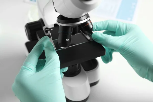 Assistente médico usando microscópio moderno na mesa branca, close-up — Fotografia de Stock