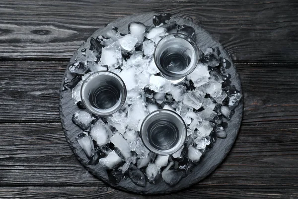 Vodka v brokových brýlích a ledu na černém dřevěném pozadí, pohled shora — Stock fotografie