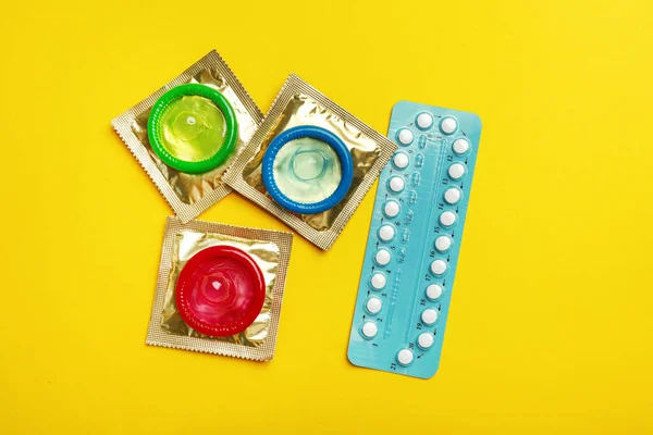 Préservatifs et pilules contraceptives sur fond jaune, à plat. Concept de sexe sûr — Photo
