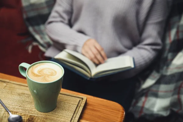 Livro de leitura da mulher na mesa, foco na xícara de café — Fotografia de Stock