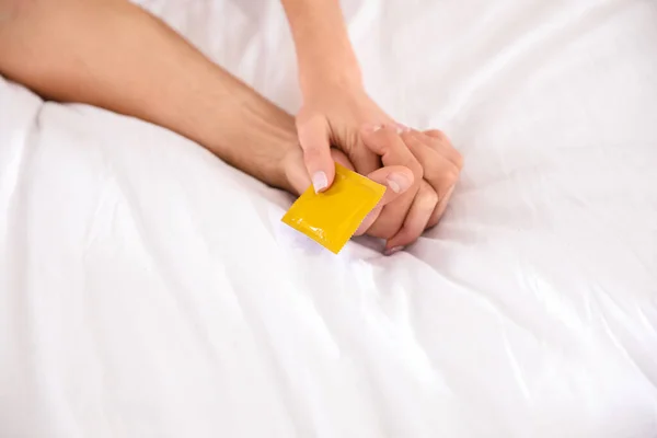 Γυναίκα και άντρας κρατούν το προφυλακτικό μαζί στο κρεβάτι, κοντά. Έννοια ασφαλούς σεξ — Φωτογραφία Αρχείου
