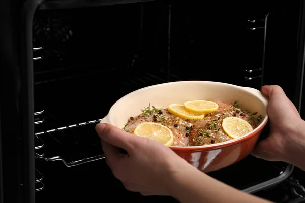 Woman putting chicken breasts with lemon and rosemary into oven, closeup — Stock Photo, Image
