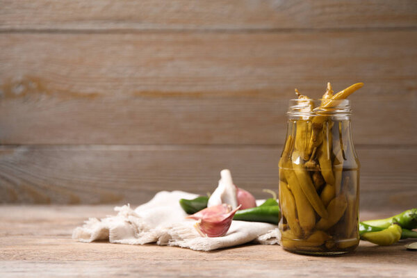 Glass jar with pickled peppers on wooden table. Space for text