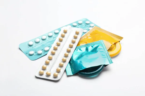 Презервативы и противозачаточные таблетки на белом фоне, крупный план. Безопасный секс — стоковое фото