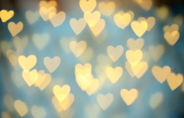 Vista turva de belas luzes em forma de coração de ouro no fundo azul claro — Fotografia de Stock