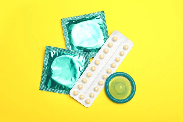 Píldoras anticonceptivas y condones sobre fondo amarillo, planas. Concepto de sexo seguro — Foto de Stock