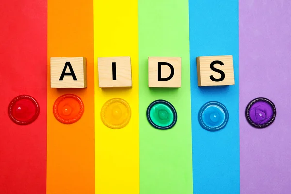 Palabra SIDA hecha con cubos de madera y condones de colores sobre fondo de arco iris, la puesta plana. Sexo seguro — Foto de Stock