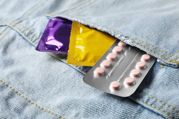 Condoms and birth control pills in pocket of jeans, closeup. Safe sex concept — Stockfoto