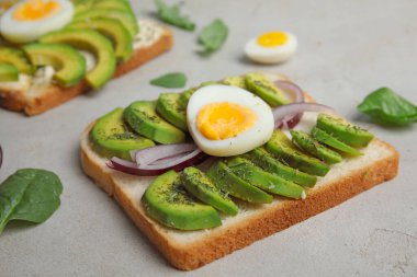 Tasty toast with avocado and quail egg served on light grey table, closeup