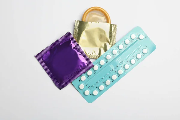 Píldoras anticonceptivas y condones sobre fondo gris claro, planas. Concepto de sexo seguro — Foto de Stock