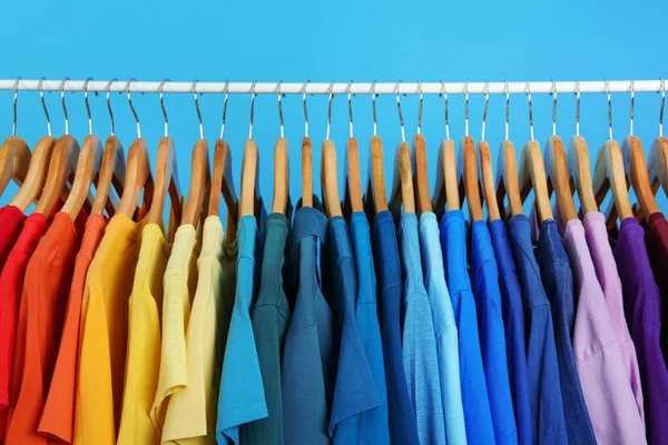 Rack met heldere kleren op blauwe achtergrond. Regenboog kleuren — Stockfoto