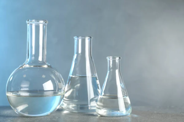 Γυάλινα αντικείμενα εργαστηρίου με υγρά δείγματα για ανάλυση σε γκρίζο τραπέζι με τονισμένο μπλε φόντο — Φωτογραφία Αρχείου