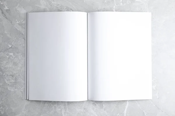 Prázdná otevřená kniha na světle šedém mramorovém pozadí, horní pohled. Vysmívat se designu — Stock fotografie