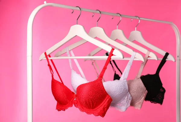 Appendini con bei reggiseni di pizzo su rack sullo sfondo rosa. Biancheria intima elegante — Foto Stock